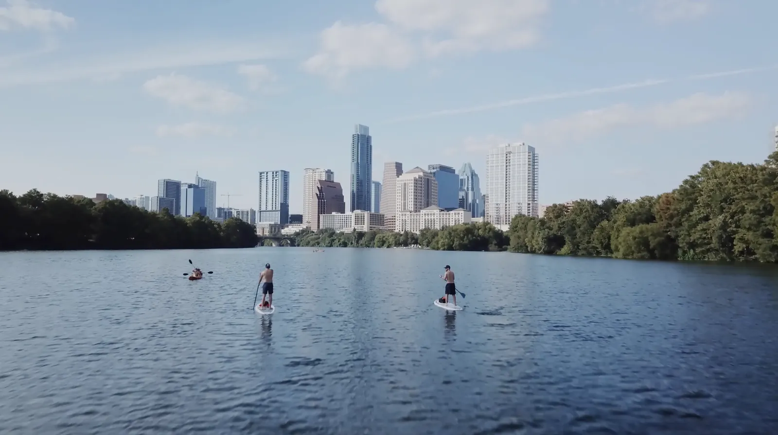 Low drone shot of paddleboarders on Lady Bird Lake with the Austin skyline behind